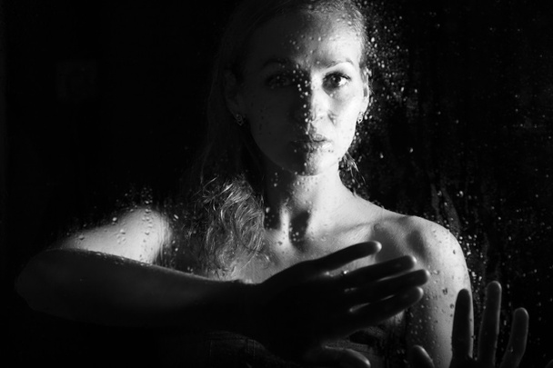 セクシーな若い女性は、水滴で覆われた透明なガラスの後ろにポーズ。憂鬱で悲しい女性の肖像画 - 写真・画像