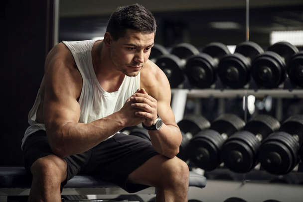 Thoughtful serious sportsman sitting in a gym - Foto, Imagen