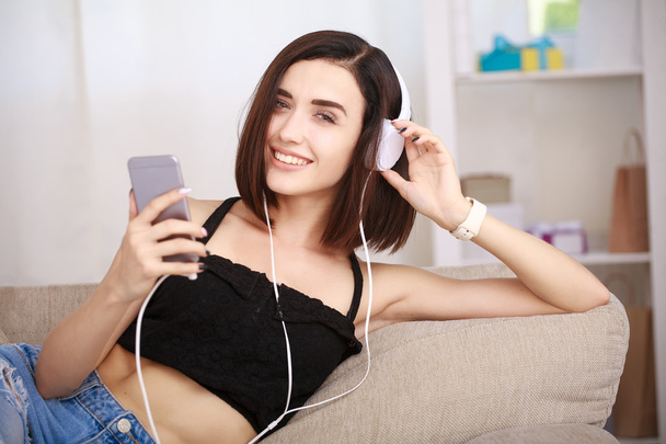 Woman listening music in headphones sitting on sofa in room - Фото, изображение