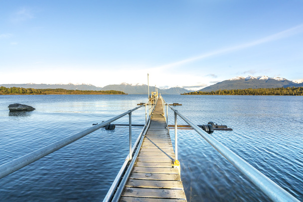 Järvi ja puinen laituri luonnollisella aamuauringon valolla
 - Valokuva, kuva
