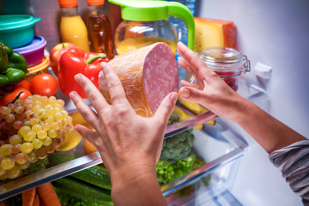 Emberi kéz nyúlt élelmiszer éjjel a nyitott hűtőbe - Fotó, kép
