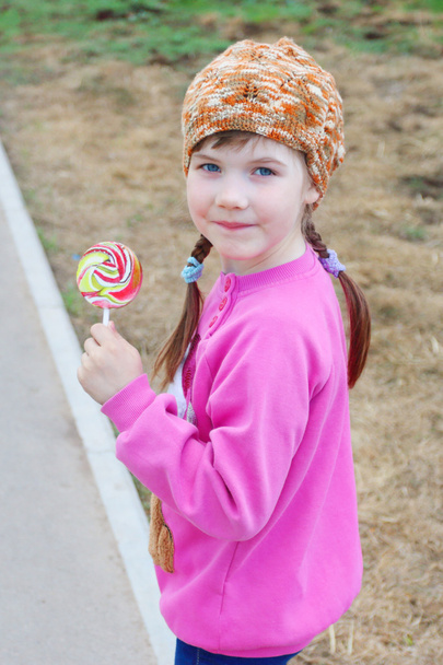 Happy little girl in pink walks with bright lollipop outdoor - Zdjęcie, obraz