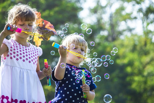 Two funny little sisters blowing soap bubbles outdoors - Photo, Image