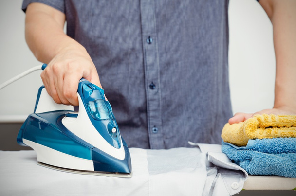 Man irons clothes on ironing board with blue iron - Φωτογραφία, εικόνα