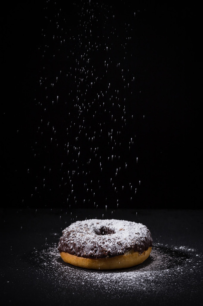 Sprinkling sugar powder on chocolate donut  - Valokuva, kuva