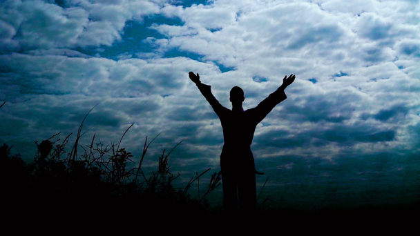 Silhouete of man stands on the stone rock with raised arms in windy day. Slowly - Footage, Video