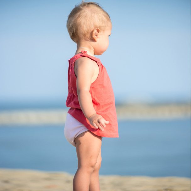 Baby girl in red dress playing on sandy beach near the sea. - Zdjęcie, obraz