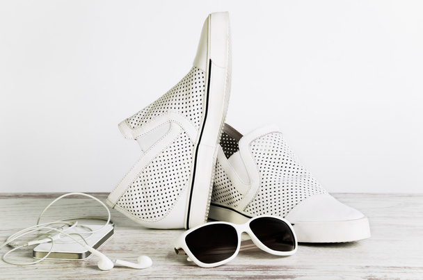 Λευκό Γυναικεία παπούτσια, γυαλιά ηλίου και ένα έξυπνο τηλέφωνο με ακουστικά - Φωτογραφία, εικόνα