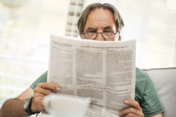 Senior man reading newspaper at home - Фото, изображение