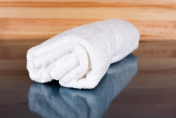 Λευκή πετσέτα σε ένα φυσικό ξύλινο υπόβαθρο με αντανάκλαση. - Φωτογραφία, εικόνα