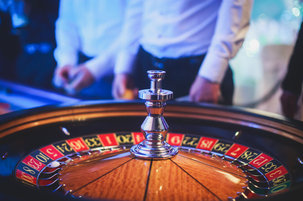 A close-up vibrant image of multicolored casino table with roulette in motion, with the hand of croupier, and a group of gambling rich wealthy people  - Φωτογραφία, εικόνα