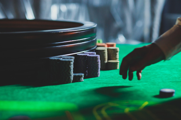 A close-up vibrant image of multicolored casino table with roulette in motion, with the hand of croupier, and a group of gambling rich wealthy people  - Photo, image