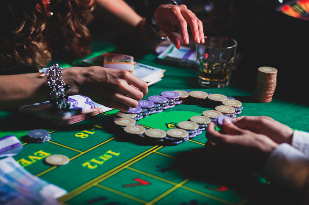 A close-up vibrant image of multicolored casino table with roulette in motion, with the hand of croupier, and a group of gambling rich wealthy people  - Photo, Image