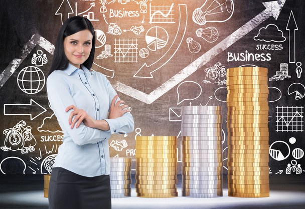 Smiling woman with black hair standing in room with giant coin stacks and blackboard with sketches. Concept of banking. Toned image - Foto, imagen