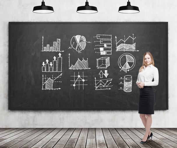 Smiling blond businesswoman with graphs on blackboard - Photo, Image