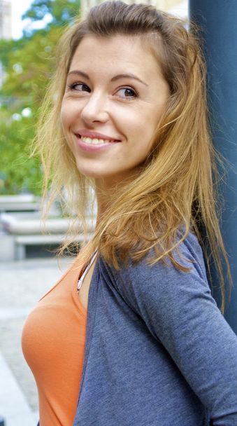 Beautiful red-haired young girl in an orange shirt with a lamp post behind poses in the city - Foto, afbeelding