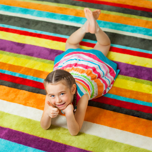 Child lying on the color carpet and showing thumbs up - Photo, Image