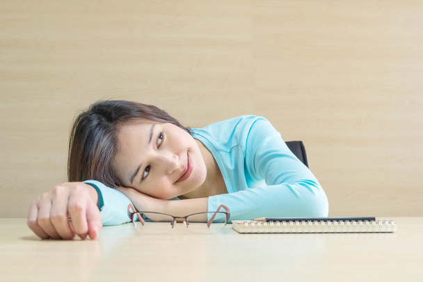 Lähikuva aasialainen nainen makasi pöydällä onnellinen kasvot lepoajalla lukemasta kirjaa hämärtynyt puinen pöytä ja seinä kuvioitu tausta kokoushuoneessa, onnellinen aika ja rentoutumista naisen käsite
 - Valokuva, kuva
