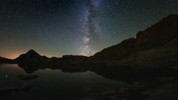 L'apparente rotazione della Via Lattea e il cielo stellato oltre il crinale innevato della montagna, riflesso sull'idilliaco lago apino. Time Lapse 4k video
. - Filmati, video