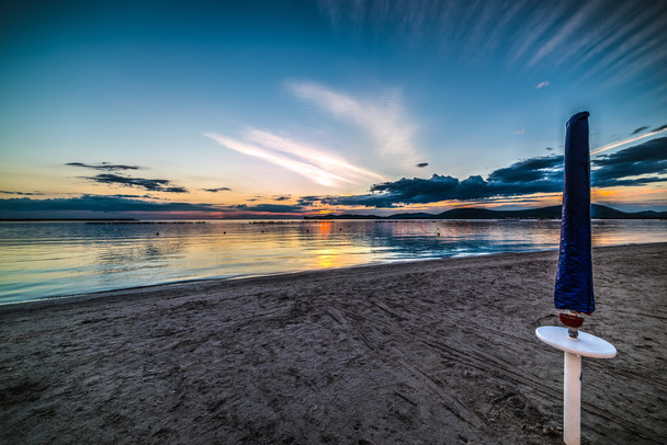 päivänvarjo yksin rannalla auringonlaskun aikaan
 - Valokuva, kuva