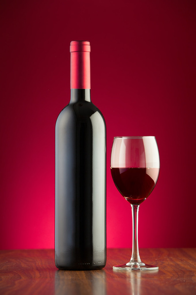 Пляшка і склянка, повні червоного вина на червоному тлі
 - Фото, зображення