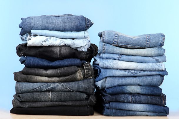 Many jeans stacked in a piles on blue background - Fotoğraf, Görsel