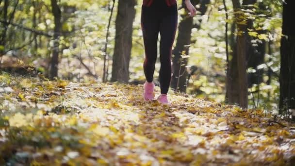 Futó fiatal lány lába futó cipő őszi út-closeup. Női fitness bikini modell szabadban ősszel a lehullott levelek borított úton kocogás. Sport egészséges életmód fogalma, lassú mozgás - Felvétel, videó