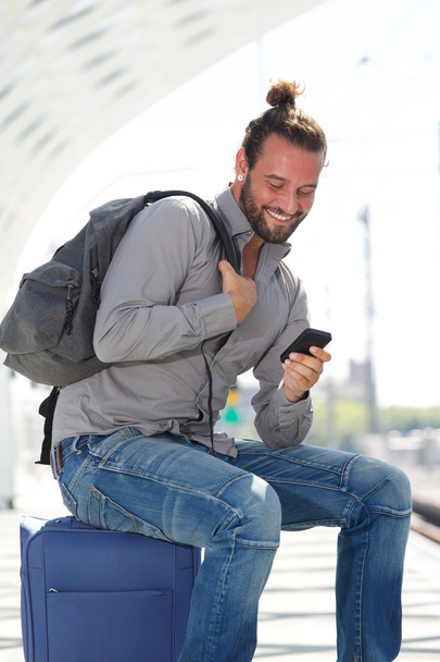 Man zit op koffer kijken naar mobiele telefoon - Foto, afbeelding