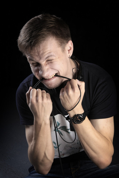 close-up portrait of a young man DJ with headphones gnaws wire on dark background studio - Φωτογραφία, εικόνα