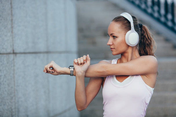 Young woman with headphones preparing for a jogging , she is stretching her arm. - Фото, зображення