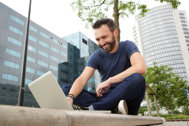 Щасливий зрілий чоловік сидить на відкритому повітрі і використовує ноутбук
 - Фото, зображення
