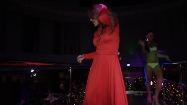 Dívka v červených šatech tančí na stojanu na párty v nočním klubu. Skok. Wave kořist. Go go - Záběry, video