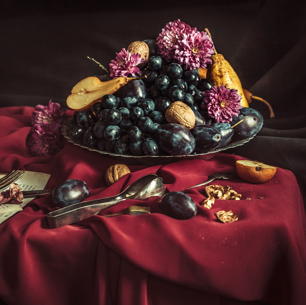 The fruit bowl with grapes and plums against a maroon tablecloth - Valokuva, kuva