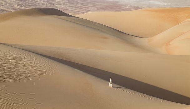 Mann in Kandura in einer Wüste bei Sonnenaufgang - Foto, Bild