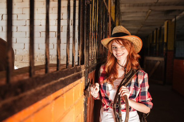 Happy beautiful young woman cowgirl standing in stable - Foto, Imagen