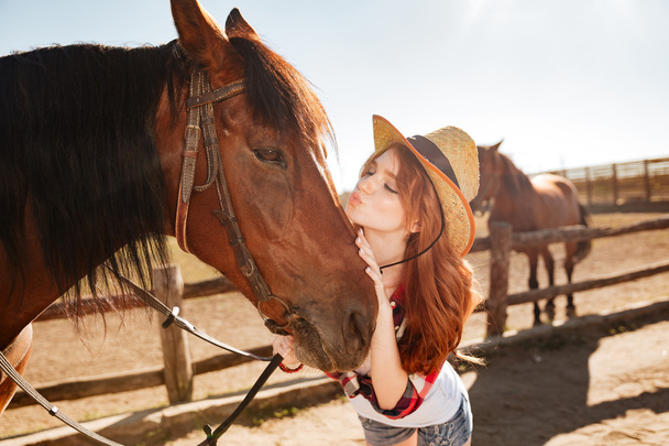 Cute woman cowgirl standing and kissing her horse - Foto, Bild