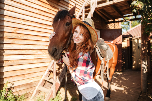 Smiling woman cowgirl in hat with her horse on farm - Photo, Image