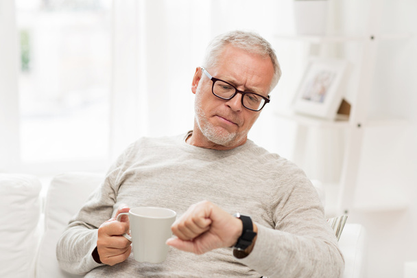 senior man with coffee looking at wristwatch - Foto, afbeelding