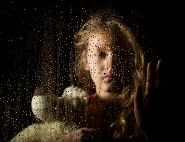 lonely young sad girl behind the window with drops, holding teddy bear and crying - Фото, изображение