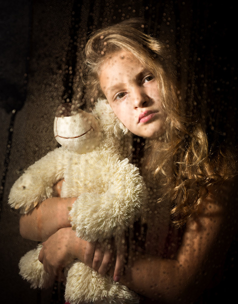lonely young sad girl behind the window with drops, holding teddy bear and crying - Фото, изображение