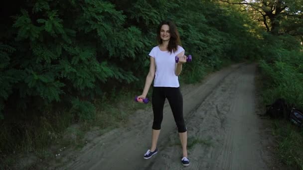 Cheerful girl lifting dumbbells in the park - Footage, Video