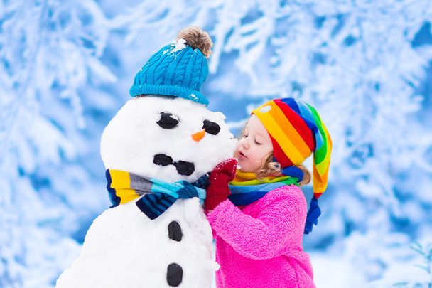Petite fille construisant un bonhomme de neige en hiver
 - Photo, image