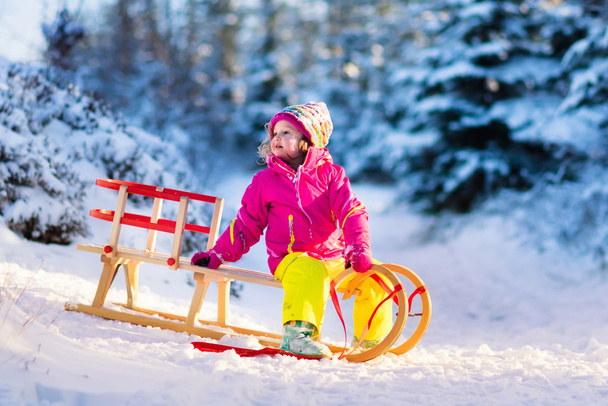 Маленька дівчинка розважається на санях у засніженому зимовому лісі
 - Фото, зображення