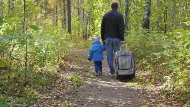 Férfi és gyermek egy bőröndöt, gyaloglás-ra egy erdei ösvényen - Felvétel, videó