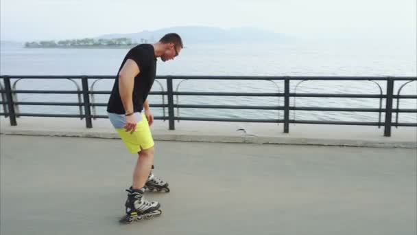 Young sporty man roller skating on summer seafront - Footage, Video