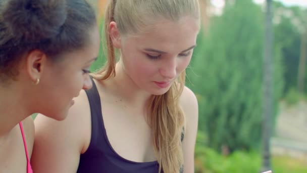 Blond dziewczyna rozmawia z afro dziewczyna w parku - Materiał filmowy, wideo