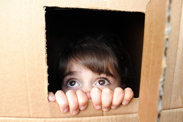 Rostro de niña asustada asomándose desde una caja de cartón
 - Foto, Imagen