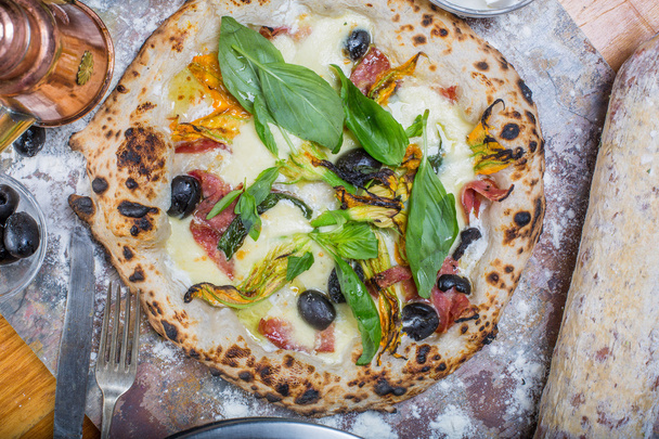 Pizza italiana tradicional con mozzarella, salami, ricotta y flores de calabaza en pizarra
 - Foto, imagen