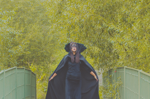 εξάπλωση του μανδύα είναι ένα κορίτσι γέφυρα σε ένα μαύρο φόρεμα και μάσκα - Φωτογραφία, εικόνα