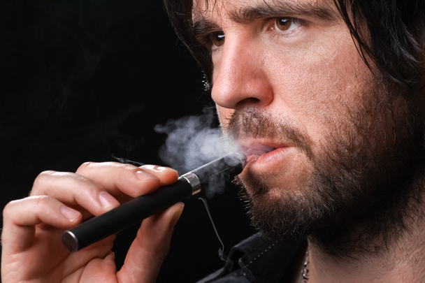 Young man smoking electronic cigarette on black background - Photo, Image